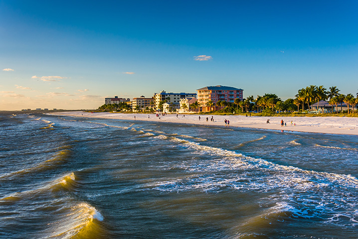 The cityscape of Fort Myers showing sunset, houses, trees, and people sunbathing on a sand beach looking onto the ocean