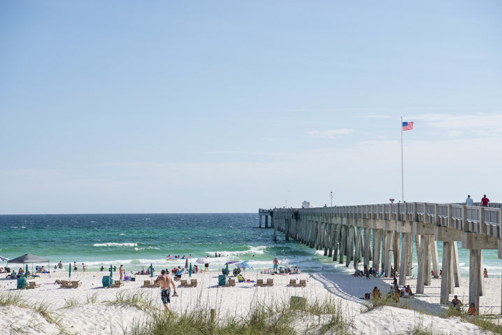 Panama City Beach fishing pier with many people sitting on a sandy beach that looks onto the ocean
